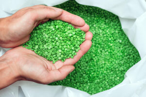 A hands hold or touching biodegradable plastic pellets, plastic polymer dye granules color clear green